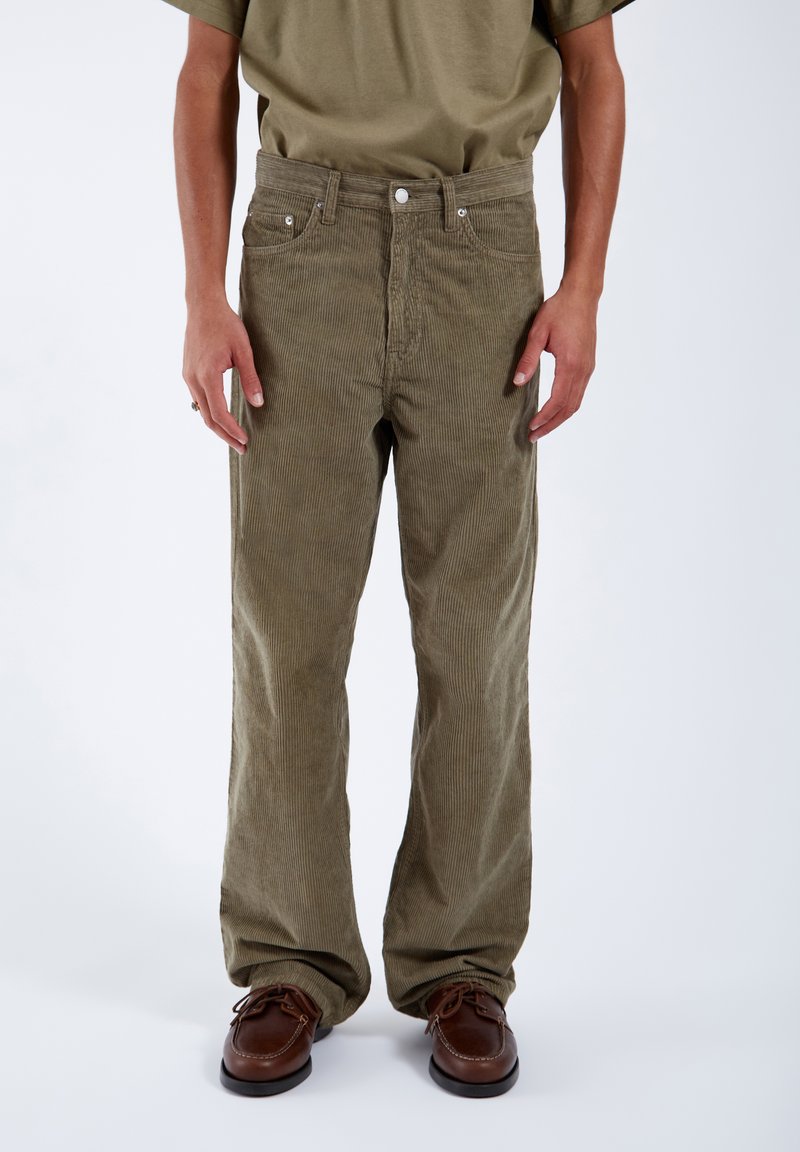Pantaloni in velluto a coste verde oliva con taglio dritto, design a cinque tasche e chiusura con bottone, indossati con scarpe stringate marroni.