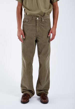 Man draagt olijfgroene corduroy broek met rechte pasvorm, gecombineerd met bruine leren schoenen en een olijfgroene overhemd.