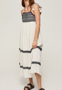 Weißes Kleid mit einem gesmockten Oberteil in schwarzmuster und schwarzen Details. Verfügt über verstellbare Träger und ein luftiges, gestuftes Design.