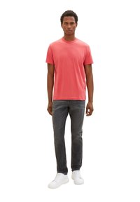 Rotes Baumwoll-T-Shirt mit Rundhalsausschnitt, kombiniert mit dunkelgrauen Jeans und weißen Sneakers. Schlichtes Design, kurze Ärmel und normale Passform.