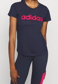 Marinblå Adidas t-shirt med en ljusrosa logotyp över bröstet; kortärmad, rund halsringning och en figurnära design.