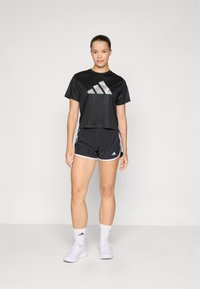 Black short-sleeve athletic shirt with reflective Adidas logo, paired with black shorts featuring white accents. Worn with white socks and shoes.