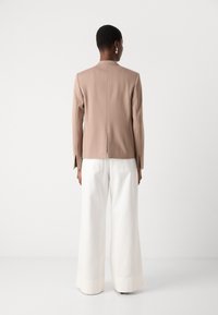 Beige tailored blazer with a fitted design and side slits, paired with wide-leg white trousers. Simple, seamless aesthetic and solid colors.