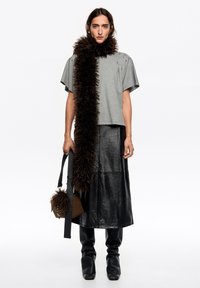 Szara koszula z krótkim rękawem z ćwiekami na ramionach, czarna skórzana spódnica i miękki brązowy szalik. Czarna torebka z futrzanym akcentem. Czarne buty na obcasie.