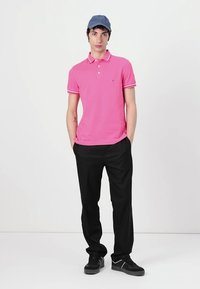 Kortärmad rosa polo med kontrasterande vita kragstreck, i kombination med svarta byxor och svarta sneakers. En blå keps fulländar outfiten.