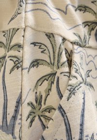Katoenen stof met een crèmekleurige achtergrond met palmbomen illustraties in donkergroen en zwart. Textured breisel met zichtbare naden.