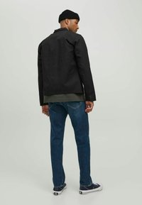 Sort jakke lavet af slidstærkt stof, med krave og knaplukning. Kombineret med blå jeans og sorte sneakers.