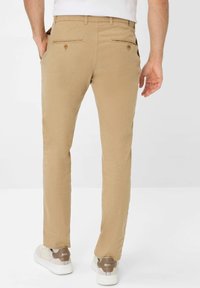 Khaki broek met een recht model, twee achterzakken met knopen en een platte voorkant. Gecombineerd met witte sneakers met een beige accent.