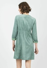 Vestido de pana verde con mangas de tres cuartos, cintura fruncida y puños enrollados. Tejido texturizado con detalle de estrías verticales.