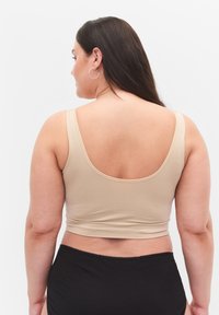Beige avkortad tanktopp med breda axelremmar som visar en jämn textur. Matchad med högmidjade svarta underdelar. Minimalistisk design.