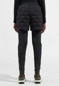 Shorts noirs isolants par-dessus des leggings noirs ajustés, tous deux fabriqués dans un matériau extensible. Les shorts ont une texture matelassée et une taille élastique.