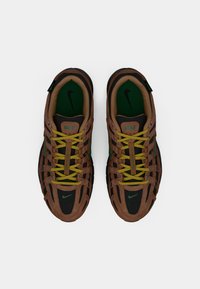 Ζευγάρι καφέ και μαύρες αθλητικές παπούτσια Nike με κίτρινες κορδόνες και πράσινα πατάκια, βλέπεται από πάνω σε λευκό φόντο.