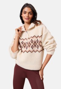 Pulover din fleece de culoare crem cu guler cu jumătate de fermoar, având un model geometric în nuanțe de roz și maro pe piept. Textură moale, croială lejeră.