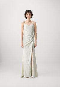 Robe de soirée longue sans manches en satin crème clair. Présente un corsage ajusté, un drapé sur le côté et une fente haute sur la cuisse.