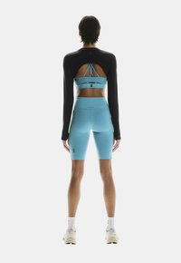 Sportstøj bestående af en sort langærmet top og lyseblå kompresionsshorts, med et stropdesign på bagsiden af toppen.
