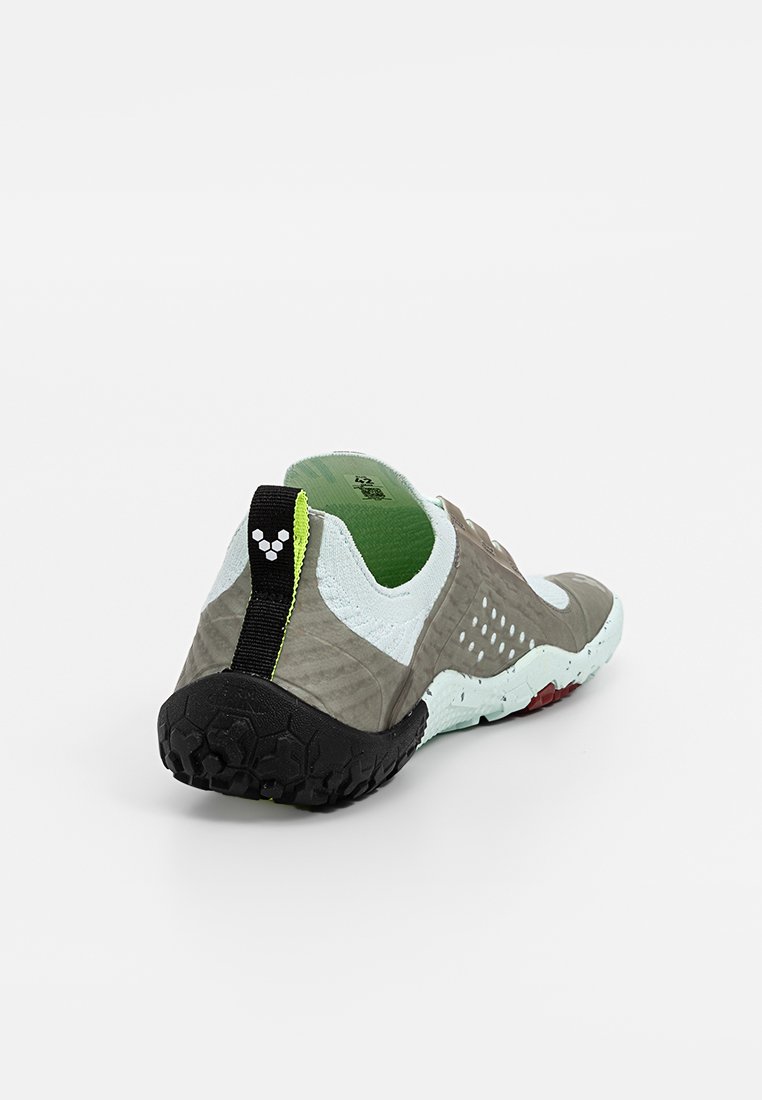 Zapatilla baja gris y blanca con suela texturizada negra, forro interior verde y lengüeta negra con un logo triangular blanco.