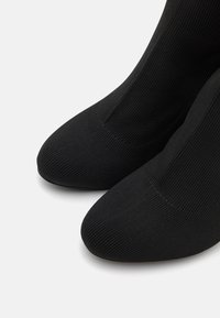 Chaussettes noires côtelées avec une conception d'orteil lisse, dotées d'une forme ajustée et d'une texture douce. Les détails incluent un orteil sans couture et une longueur à la cheville.