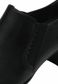 Černý kožený kotník s hladkou strukturou, elastickým bočním panelem se zvlněným detailem a umírněným podpatkem.