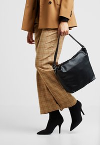 Svart läderhandväska med texturerad yta, kombinerad med tanrutig vida byxor och svarta spetsiga stilettklackar.