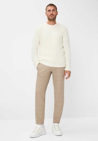 Crème ribbel gebreide trui, beige geruite broek en witte sneakers. De outfit heeft een relaxte pasvorm en gestructureerde materialen.