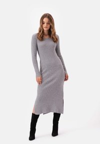 Szara sukienka dzianinowa w prążki z długimi rękawami, bocznymi rozcięciami i dopasowanym krojem, zestawiona z czarnymi botkami do kolan.