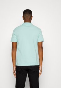 Camisa polo verde menta de manga corta y cuello clásico, hecha de suave algodón. El diseño presenta un dobladillo recto y un detalle mínimo.