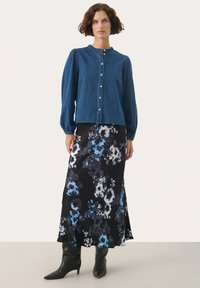 Denim košeľa s gombíkmi, okrúhlym výstrihom a balónovými rukávmi, skombinovaná s dlhou čiernou sukňou s kvetinovým vzorom, obsahujúcou modré a biele akcenty.