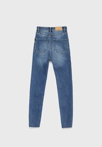 Jean en denim bleu skinny avec cinq poches, taille haute et décoloration légère. Présence d'une étiquette en cuir marron à l'arrière de la taille.