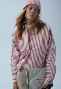 Różowa i biała koszula w paski na guziki o luźnym kroju, lekkim materiale i oversize'owych rękawach, zestawiona z miękką różową czapką beanie.