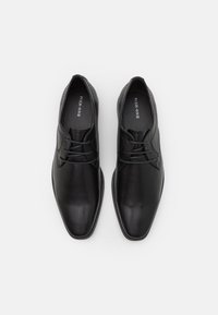 Chaussures de ville noires en cuir avec une texture lisse, un design à bout pointu et un système de laçage. Présente un logo discret à l'intérieur.
