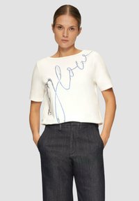 Biała koszula z krótkim rękawem z niebieskim koralikowym wzorem na przodzie. Połączona z ciemnoszarymi eleganckimi spodniami. Gładka tekstura.