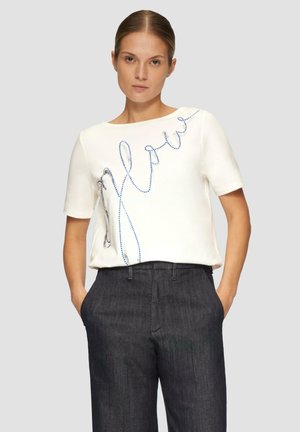Chemise blanche à manches courtes avec un design de script perlé bleu sur le devant. Associée à un pantalon noir à la coupe ajustée. Texture lisse.