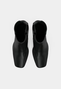 Bottes en cuir noir à la cheville avec un design élégant, un bout pointu, une texture lisse et une fermeture éclair sur le côté.