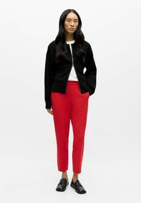 Schwarze Jacke mit Reißverschluss, weißes Hemd, rote maßgeschneiderte Hose und schwarze Loafers. Glatter Stoff mit entspanntem Schnitt, gerades Bein-Design.