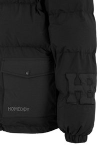 Giacca a vento nera con finitura testurizzata. Presenta una grande tasca con bottone a pressione, logo ricamato "HOMEBOY" e una lettera "H" cucita sul maniche.