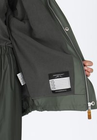 Grøn, vandtæt jakke med blødt gråt fleecefor indeni. Har lynlåslukning, elastisk talje og et plejelabel fastgjort.