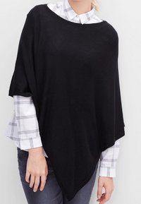 Poncho noir en tissu doux, doté d'un large col, d'un ourlet asymétrique, porté sur une chemise à carreaux blanche. Texture lisse, design décontracté.