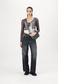 Schwarze High-Waist-Jeans mit lockerer Passform, kombiniert mit einem verkürzten, transparenten Karo-Top und einer grauen Umhängetasche. Klobige schwarze Schuhe runden den Look ab.