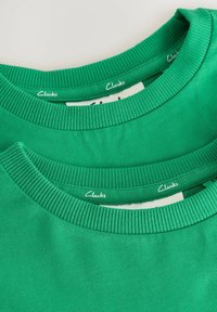 T-shirts en coton vert empilés, avec des cols côtelés et des étiquettes "Clarks" près du cou. Texture lisse avec une couleur unie.