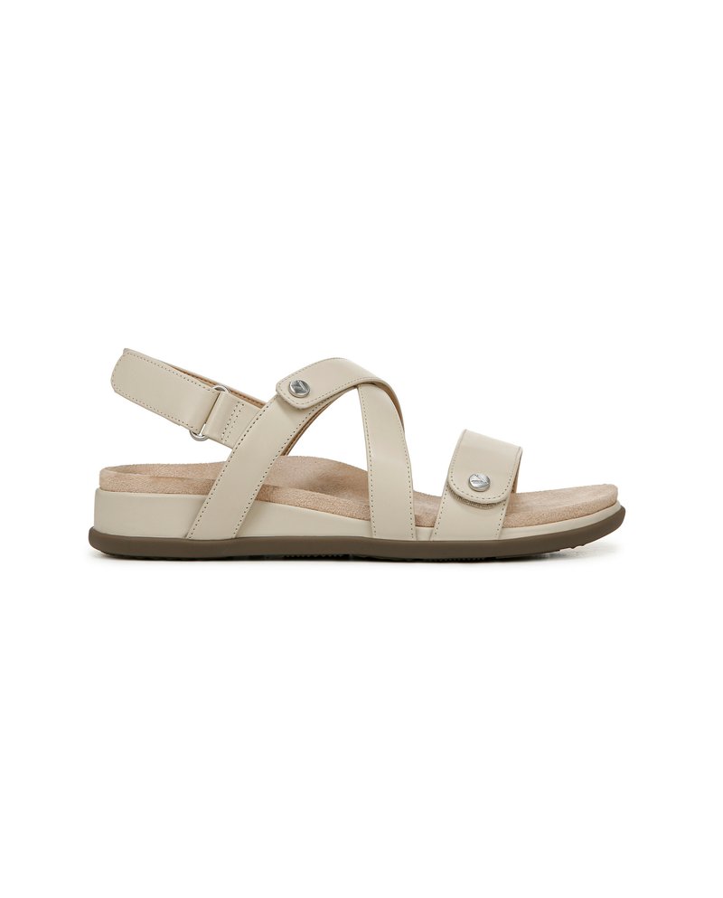 Beige sandaal met een textuur voetbed, verstelbare riemen en metalen accenten. Heeft een platte zool met een gewatteerde binnenzool voor comfort.