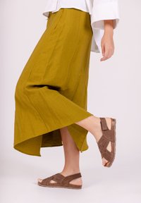 Gonna midi verde oliva, morbida e svasata, con uno spacco alto. Sandali marrone con fasce in suede e suola testurizzata.