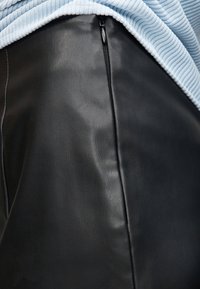 Κοντινό πλάνο μαύρου δερμάτινου ρούχου με κάθετη λεπτομέρεια φερμουάρ, σε συνδυασμό με ανοιχτό μπλε ριμπ ύφασμα από πάνω.