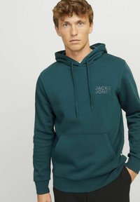 Capuchon sweatshirt in donkergroene stof, met een voorzak in kangoeroestijl en een klein logo op de borst. Standaard pasvorm met ribgebreide manchetten.