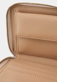 Interno di un portafoglio in pelle beige con chiusura a zip, dotato di scomparti per carte e una texture liscia. I dettagli cuciti accentuano i bordi.