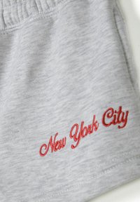 Grijze shorts van zacht materiaal met een rode geborduurde tekst "New York City" op de voorkant. Zichtbare elastische tailleband en steken details.