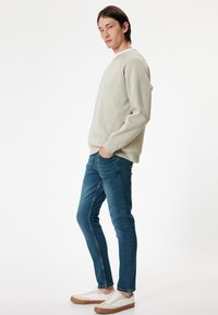 Ljusgrå sweatshirt med rund halsringning, tillsammans med slim-fit blå jeans och vita sneakers med bruna sulor. Texturen är slät.