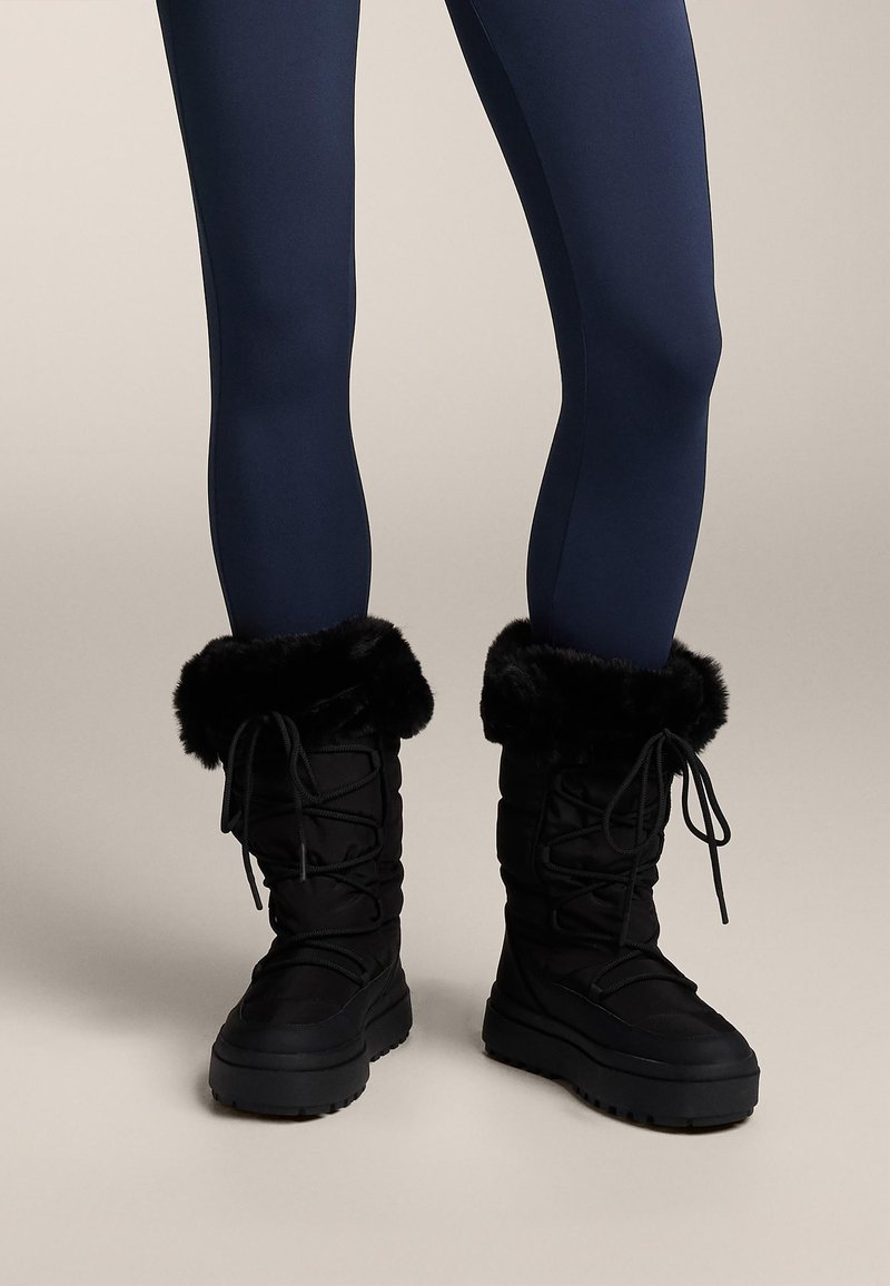 Čierne snehové čižmy s manžetami z umelého kožušiny, so šnurovaním, hrubou podrážkou a polstrovanou látkou pre teplo a pohodlie.