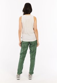 Top senza maniche di colore chiaro con un dettaglio arricciato sul retro, abbinato a pantaloni cargo verdi, larghi e con una texture, e sneakers grigie.