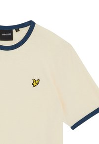 Creme t-shirt med en navy ribbet krave. Har et lille broderet gult fuglelogo på venstre bryst. Blødt bomuldsstof.