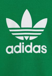 Green cotton T-shirt featuring a large white Adidas logo with three leaves and three horizontal stripes above the word "adidas."